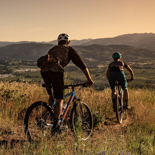 Two people riding with mountain bike gear attached to their bikes.